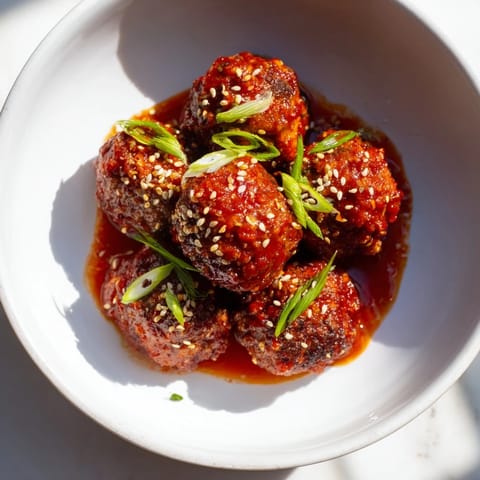 Close-up of Spicy Sriracha Honey Meatballs garnished with sesame seeds and green onions on a platter.