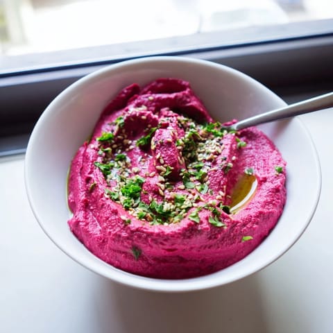 Roasted beet hummus topped with sesame seeds and fresh herbs, ready for dipping with colorful vegetable sticks.  