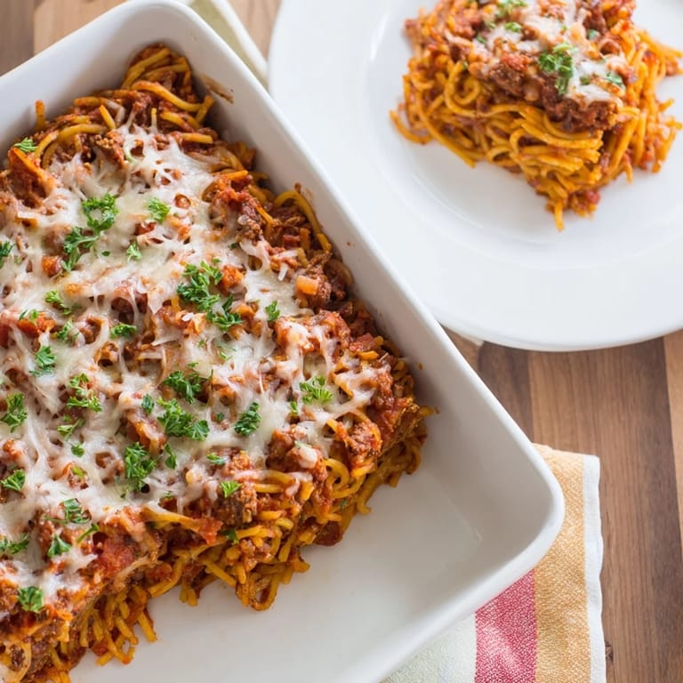 A generously portioned, steaming plate of Tinis Baked Spaghetti, ready to be enjoyed with garlic bread.