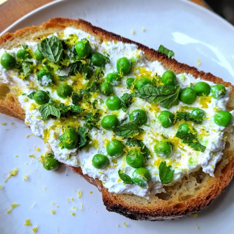 Bright green peas and fresh mint blend into smooth ricotta on toasted sourdough, finished with lemon zest for a vibrant breakfast.