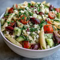 A colorful Greek pasta salad with feta, olives, and fresh vegetables, perfect for summer picnics.